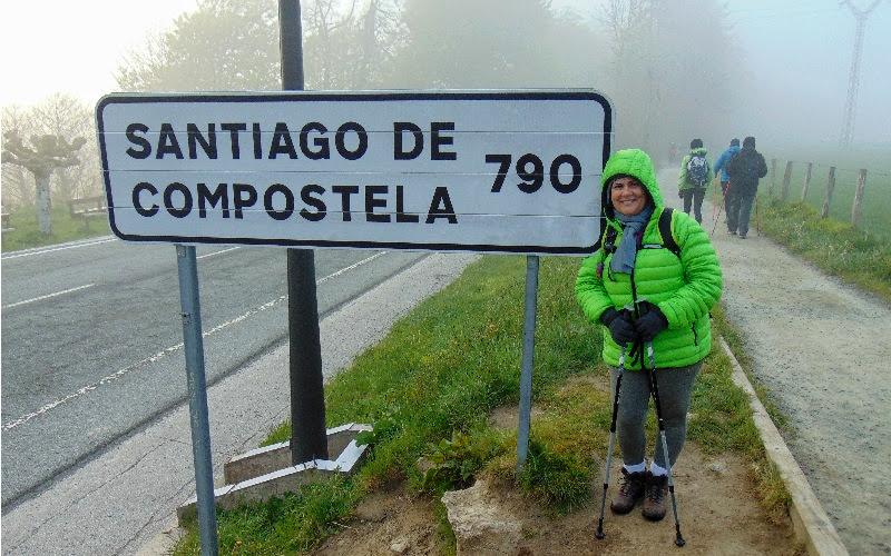 peregrina ao lado da placa sinalizando a distância de 790 km para Santiago de Compostela