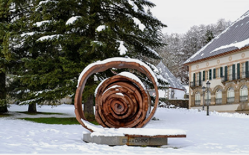 escultura circular e espiralada em ferro num jardim coberto de neve