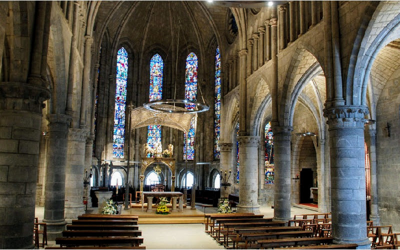 interior de igreja construída e adornada por arcos e colunas de pedra e vitrais coloridos