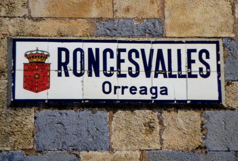 Placa em azulejo branco, com o brasão e o nome Roncesvalles Orreaga pintado em azul escuro