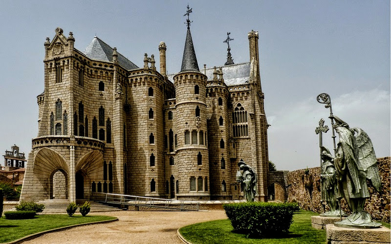 palácio construído em pedra com cruzes sobre torres, na cidade de Astorga e rodeado por um jardim com estátuas de anjos