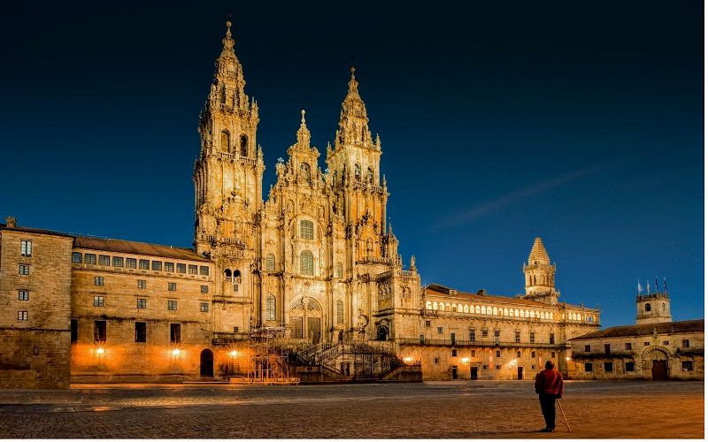 homem solitário observando a fachada da Catedral de Santiago de Compostela, na Praça do Obradoiro, ao anoitecer