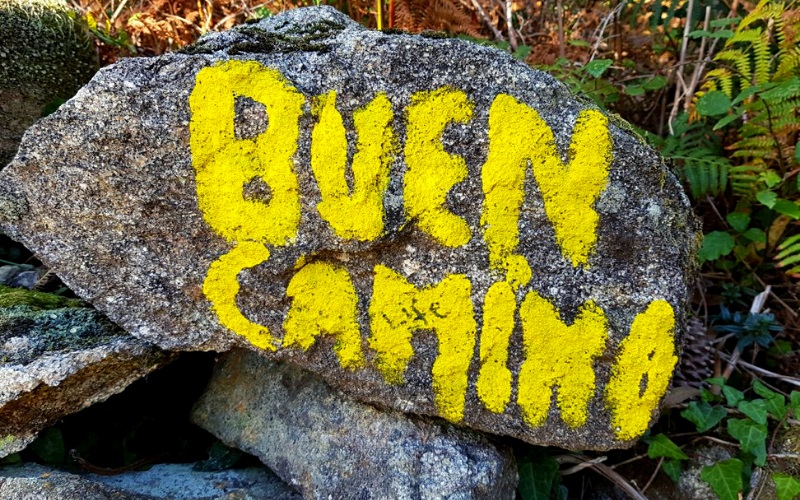 frase buen camino escrita em amarelo sobre uma pedra