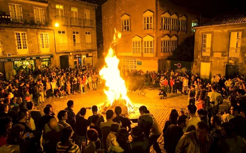 fogueira rodeadas por um grande grupo de pessoas em uma praça comemorando a festa de são joão na galicia