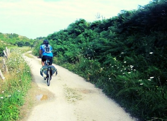 ciclista transitando em um caminho cercado por área verde de terra