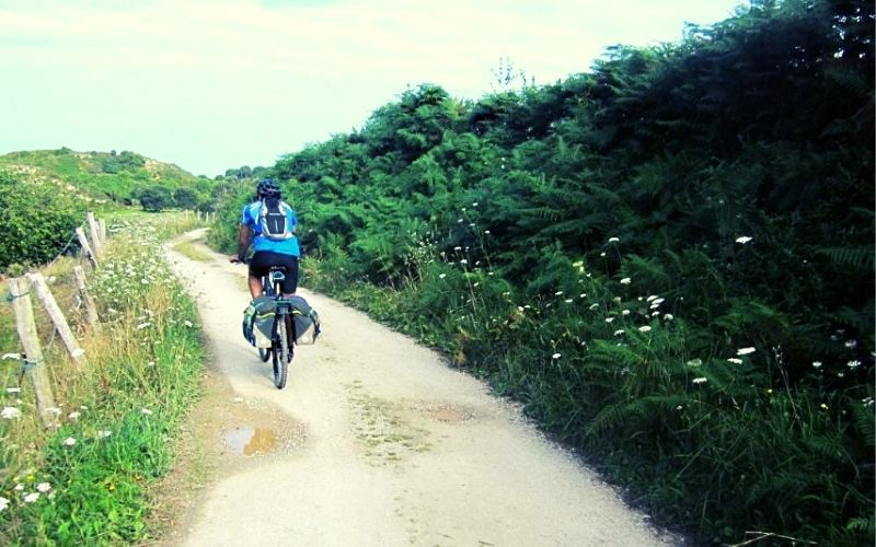 ciclista transitando em um caminho cercado por área verde de terra