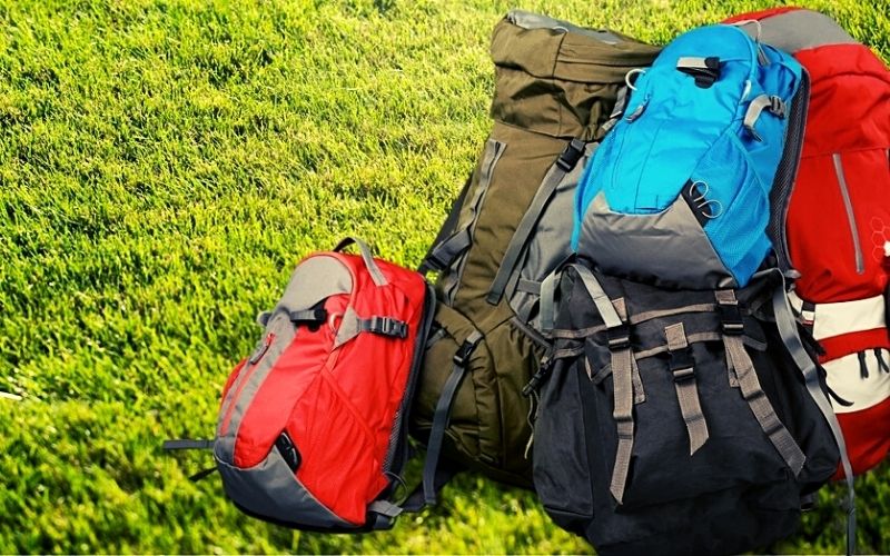 várias mochilas coloridas empilhadas sobre um gramado