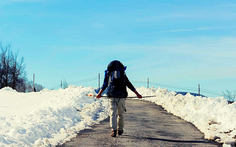 homem caminhando em dia de céu azul e margens da estrada cobertas de neve