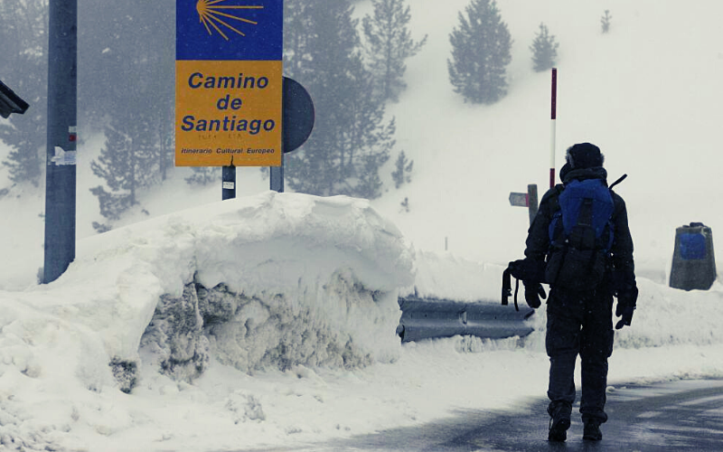 homem de costas caminhando em trilha coberta de neve no Caminho de Santiago
