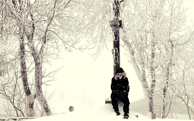 pessoa sentada aos pés de um crucifixo em paisagem totalmente coberta de neve