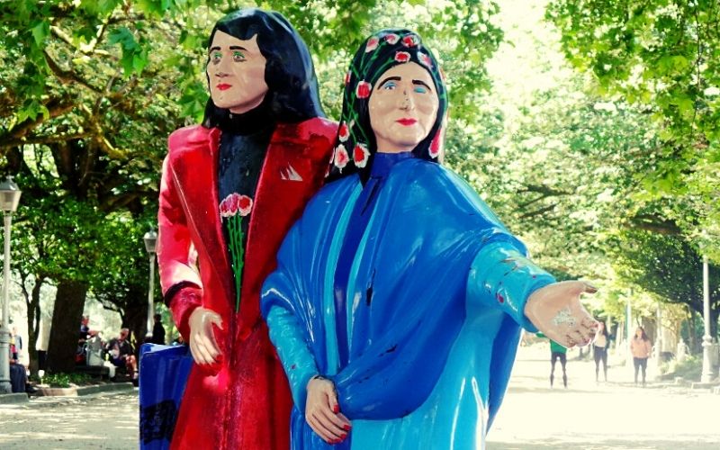 escultura de duas mulheres uma vestindo um casaco vermelho e a outra um azul 