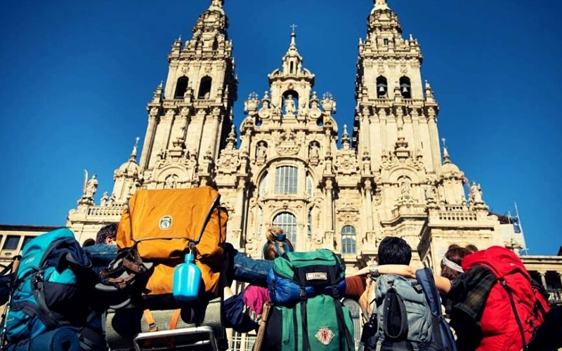 grupo de peregrinos de costas, de mochilas, em frente a Catedral de Santiago de Compostela