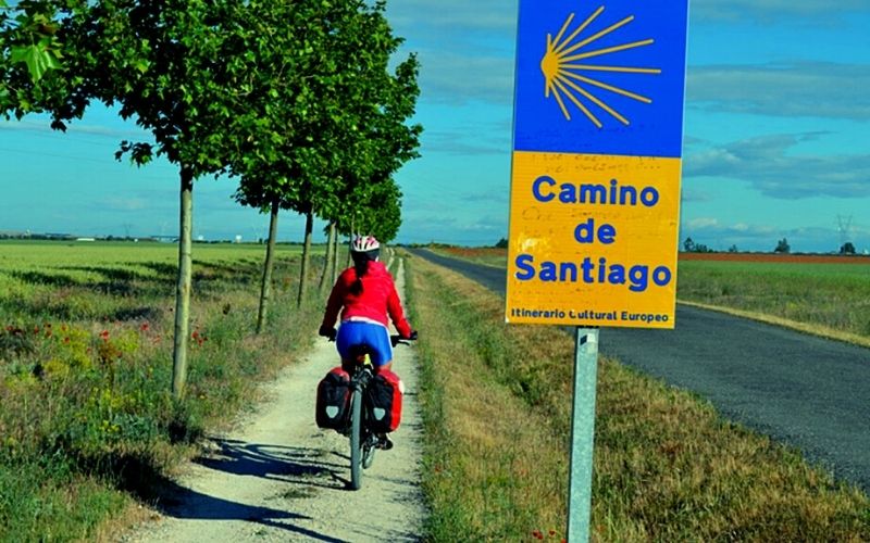 ciclista trafegando em um caminho estreito e uma placa indicando o Caminho de Santiago