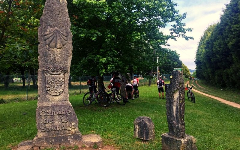 grupo de ciclista em uma área gramada com marcos de pedra que indicam o Caminho de Santiago