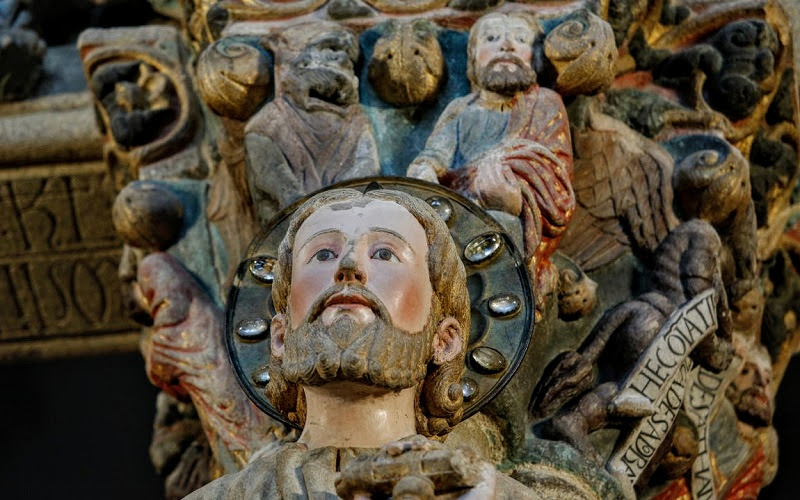 detalhe de uma escultura policromada com a face de Santiago rodeada de outras figuras humanas