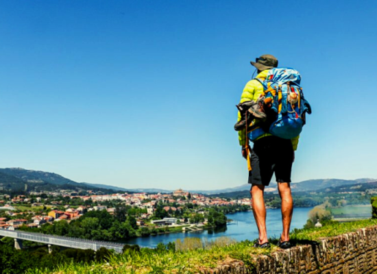 homem com mochila do Caminho de Santiago nas costas observando do alto uma paisagem à beira de um rio
