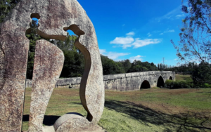 escultura vazada em pedra de um peregrino e ao fundo uma ponte medieval