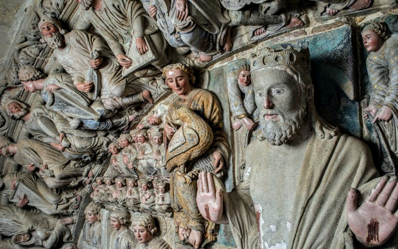 parte das esculturas do portico da gloria, na entreda da catedral de santiago de compostela, com a imagem de jesus cristo cercado de anjos e santos entalhados em pedra pintada