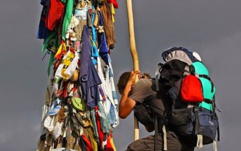peregrino ajuaelhado ao pé de um mastro cheio de fitas, tecidos e objetos coloridos