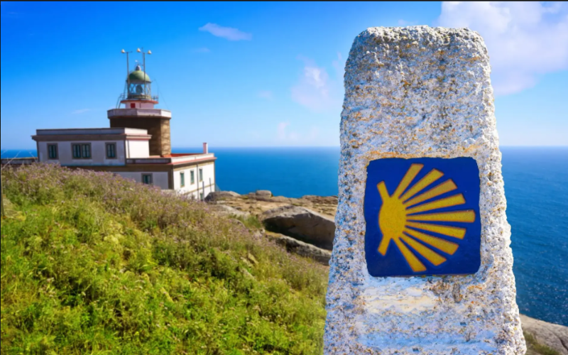 marco de pedra sinalizando o quilometro zero do caminho de santiago de compostela tendo ao fundo o farol de finisterra sobre um penhasco à beira do mar