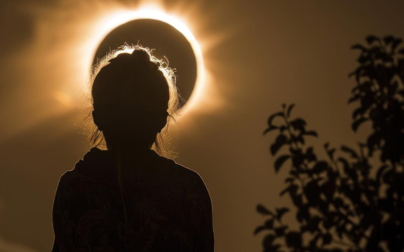 silueta de uma pessoa observando um eclipse solar em uma imagem com tons marrons e alaranjados