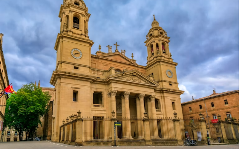 igreja cor de tijolo com duas torres laterais e um portal com três arcos, cercada por grade de ferro