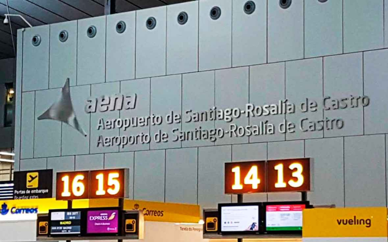 painel interno com o nome do aeroporto de santiago de compostela - rosalia de castro, com balcões com luzer acesas
